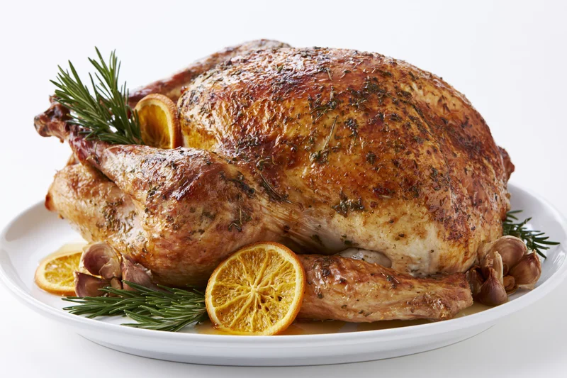 Whole roasted turkey garnished with rosemary and orange slices on a white ceramic platter