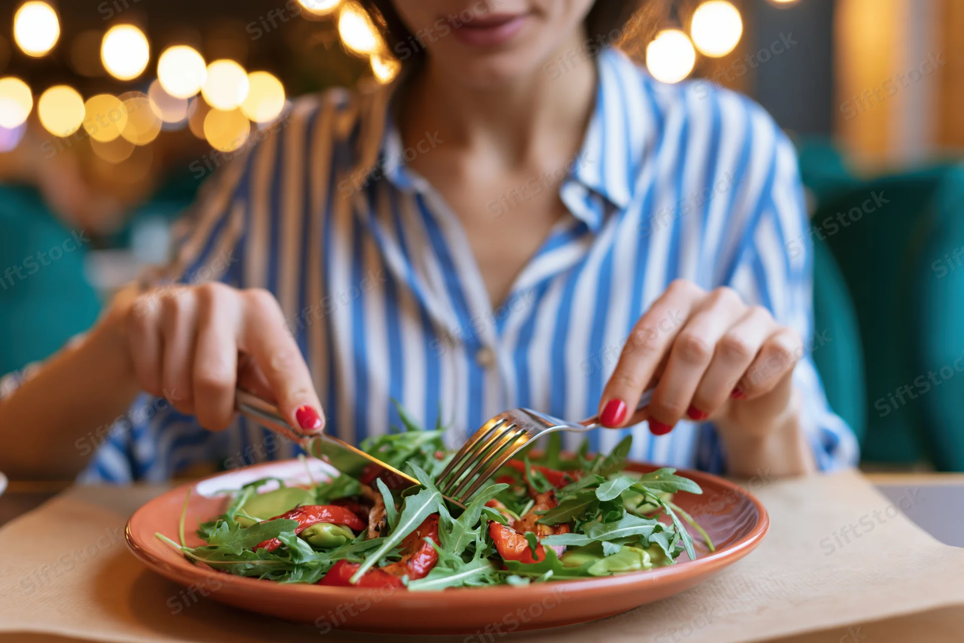 Woman eating grilled vegetable salad with fork and knife at restaurant table