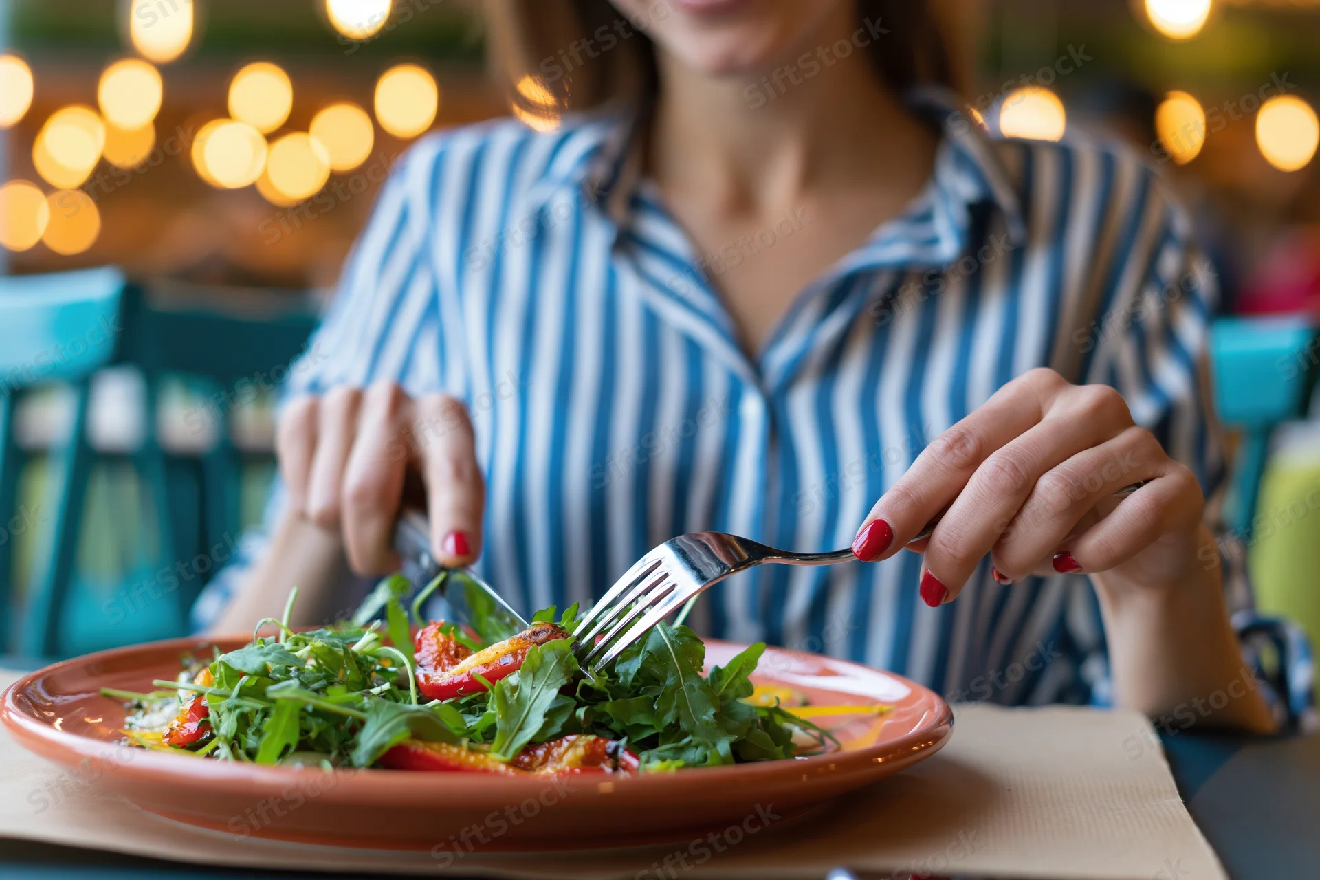 Woman eating grilled vegetable salad with fork and knife at outdoor restaurant table