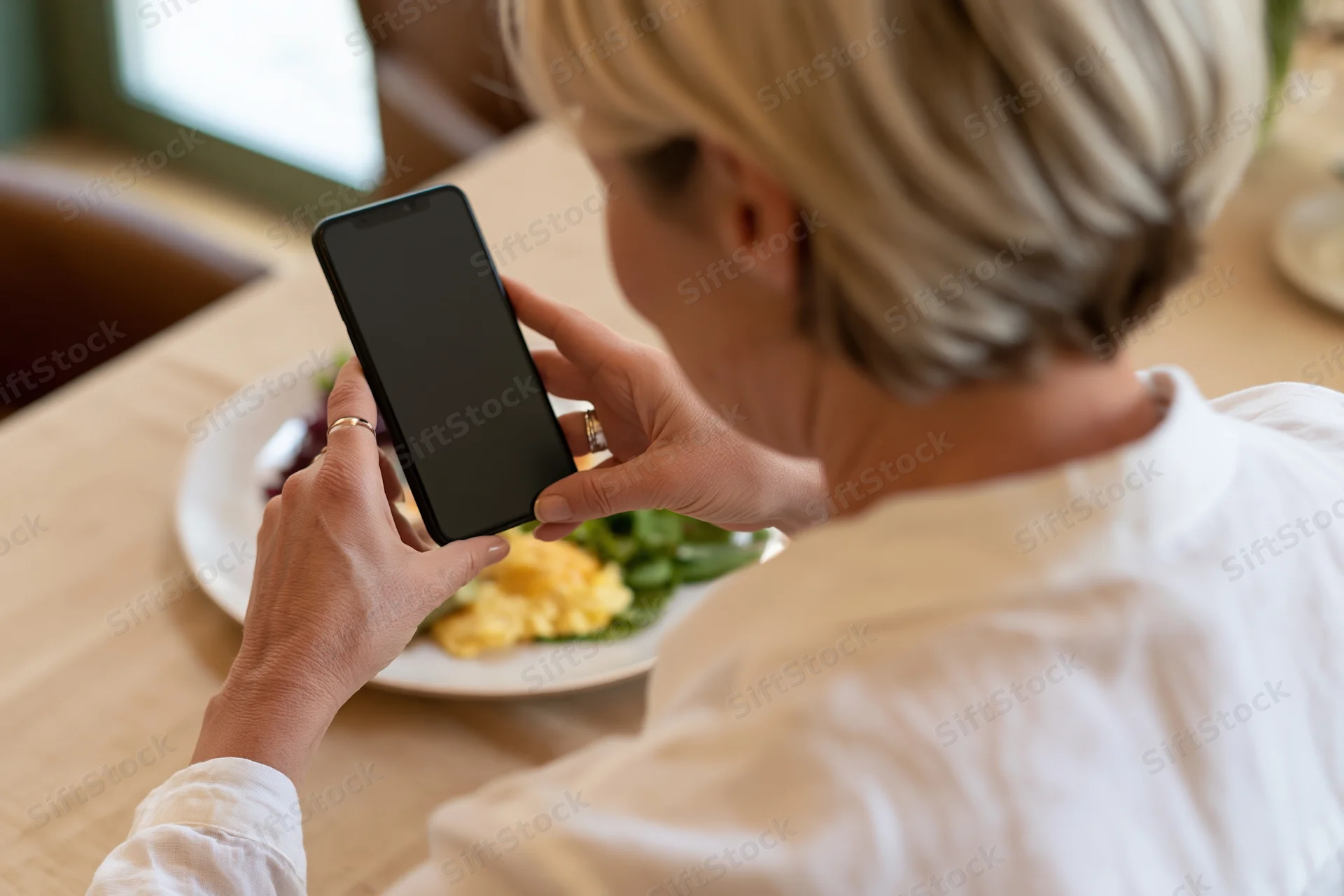 Woman holding smartphone over breakfast plate in restaurant