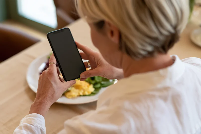 Woman holding smartphone over breakfast plate in restaurant