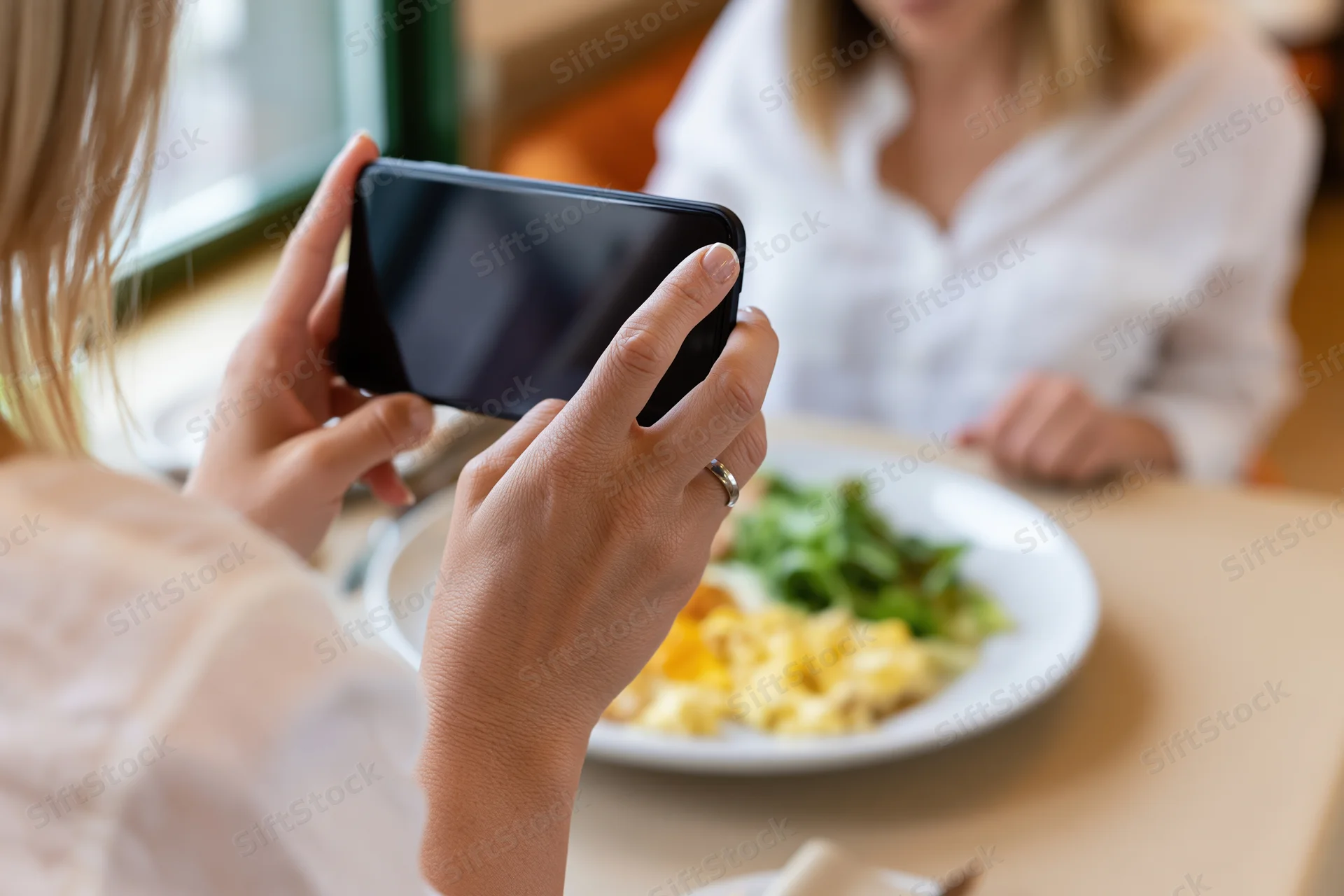 Woman holding smartphone over breakfast plate in restaurant