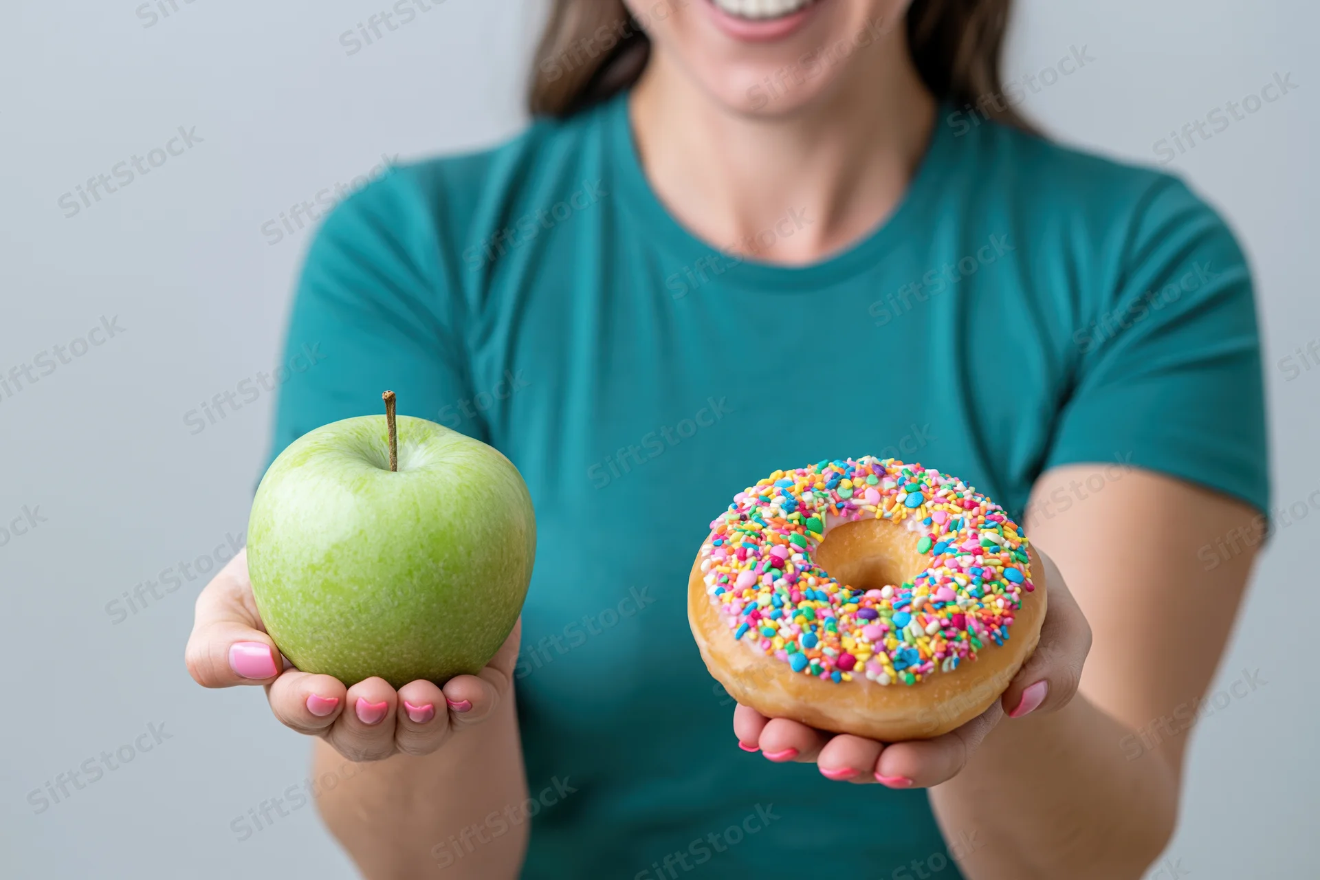 Woman holding a green apple and a sprinkled donut, smiling, in a teal tshirt