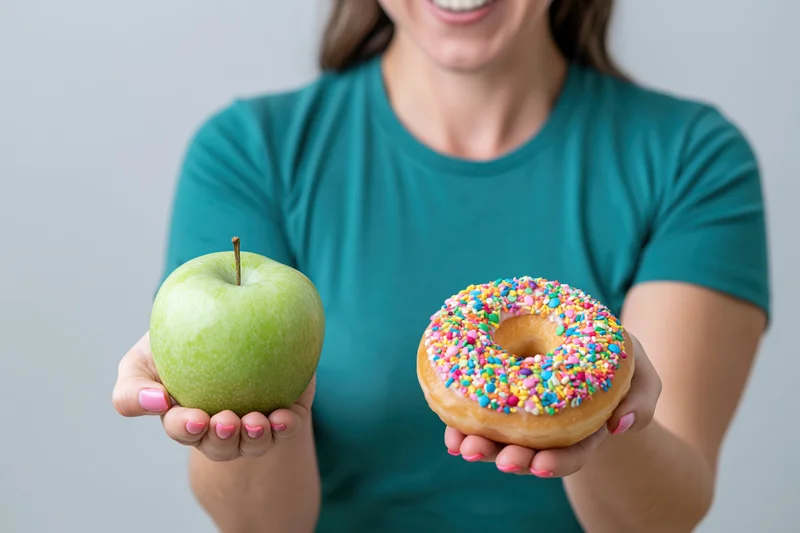 Woman holding a green apple and a sprinkled donut, smiling, in a teal tshirt