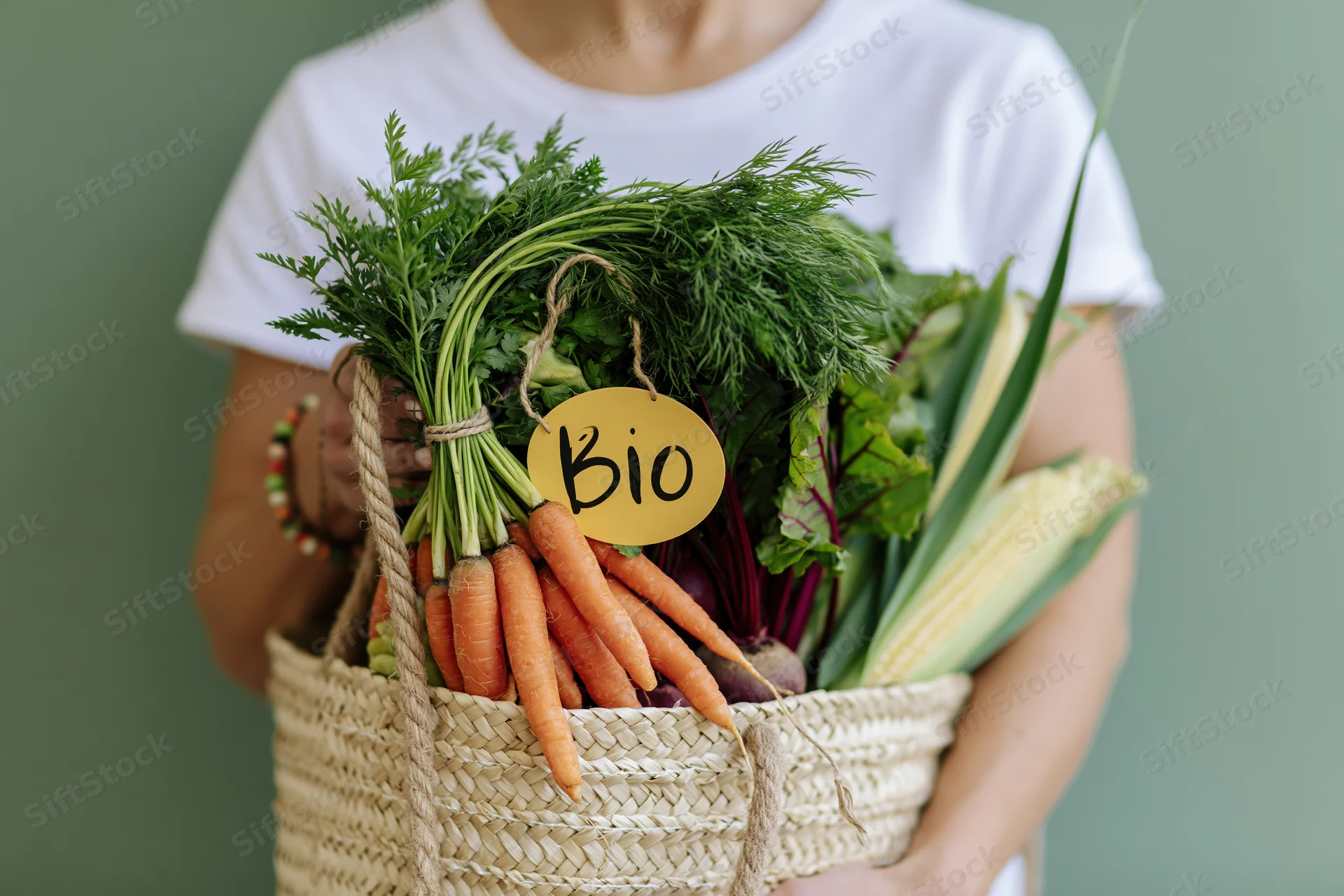 Woman holding a woven straw tote bag filled with fresh organic vegetables and herbs
