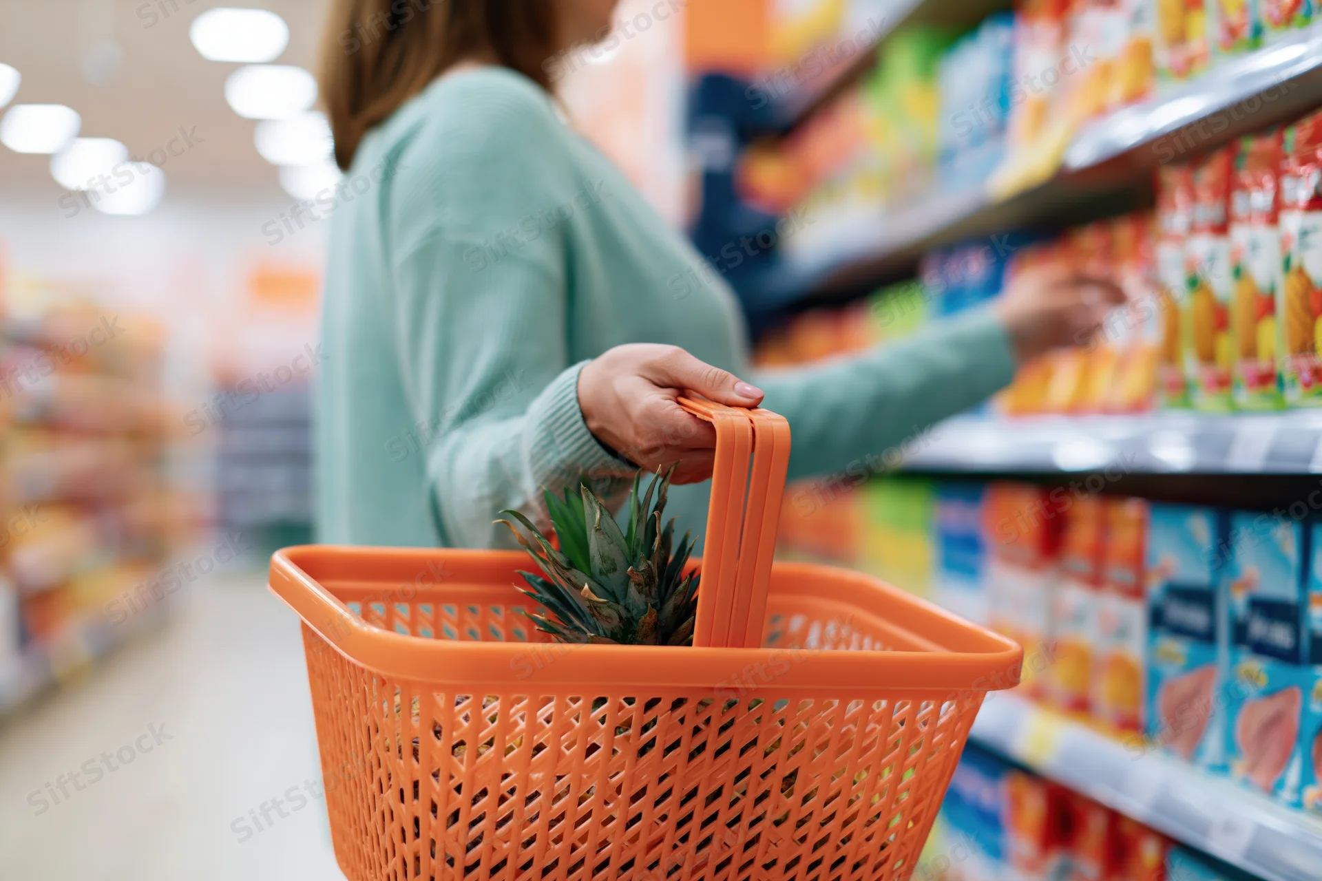Woman holding orange shopping basket with pineapple in grocery store aisle