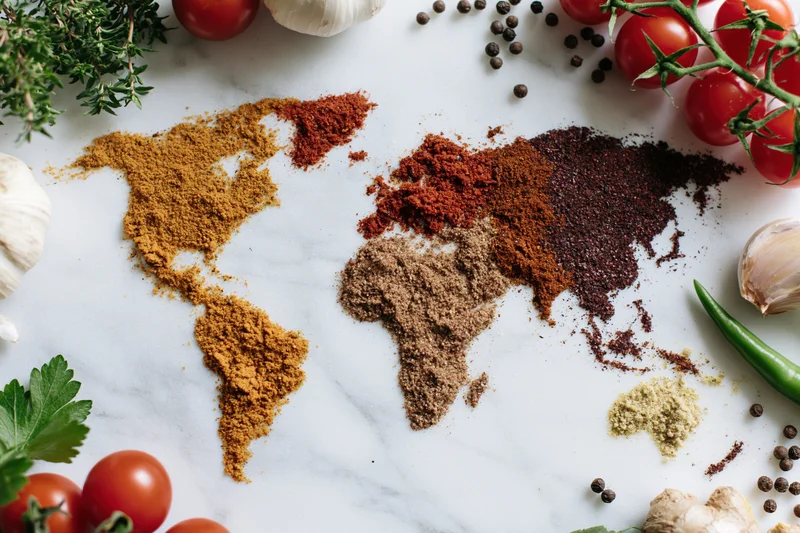 World map formed from ground spices arranged on marble surface surrounded by fresh herbs and vegetables