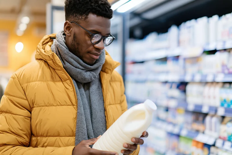Young black man reading milk bottle label in supermarket aisle