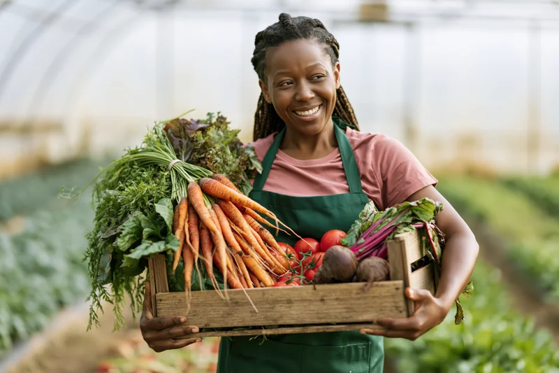Woman holding wooden crate full of fresh vegetables in greenhouse