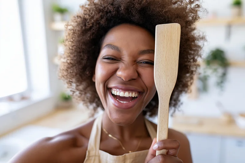 Black woman laughing while holding wooden spatula in kitchen