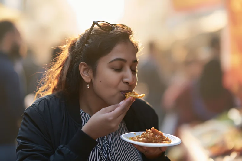 Young southasian woman eating street food from a paper plate outdoors at golden hour