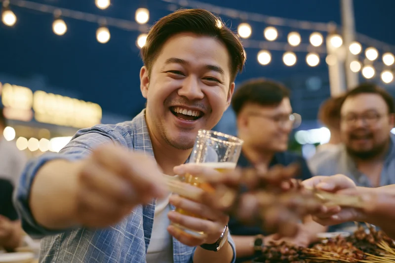 Smiling man toasting with beer glass at outdoor night party with friends
