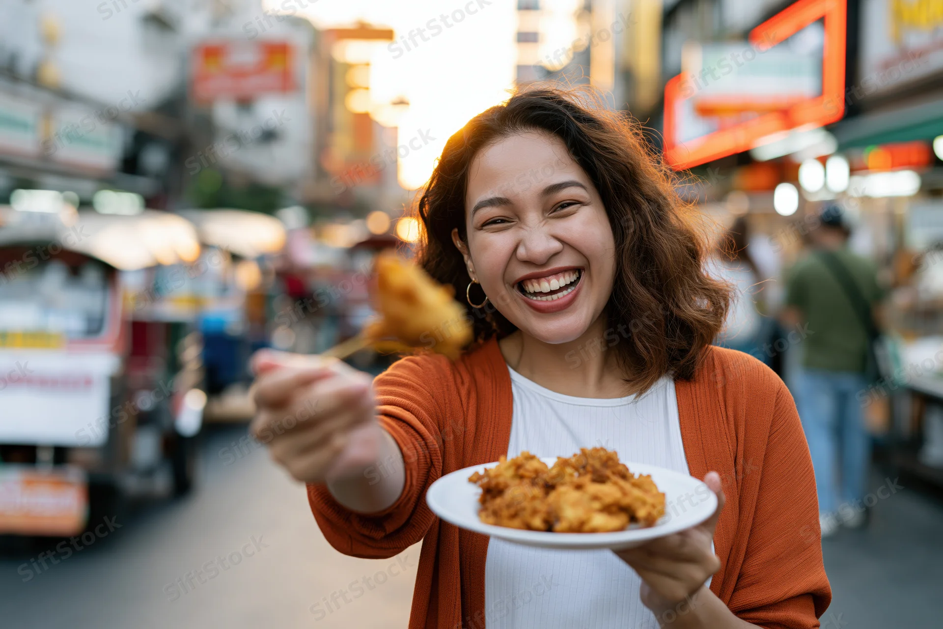 Young southeast asian woman smiling while holding plate of fried chicken in busy street market at night