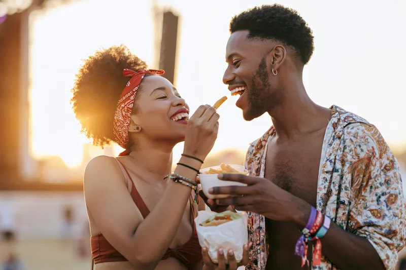 Young couple laughing and sharing street food at a summer festival outdoors