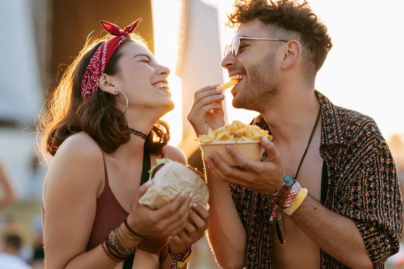 Young couple laughing and eating street food at a summer festival outdoors