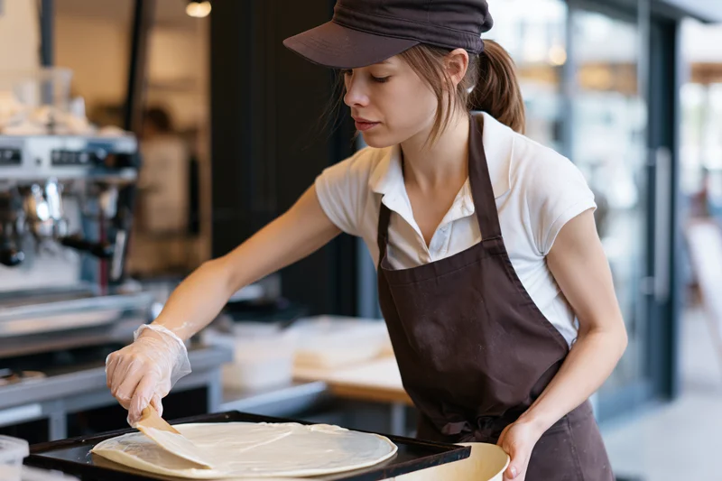 Woman spreading batter on a crepe in a cafe kitchen