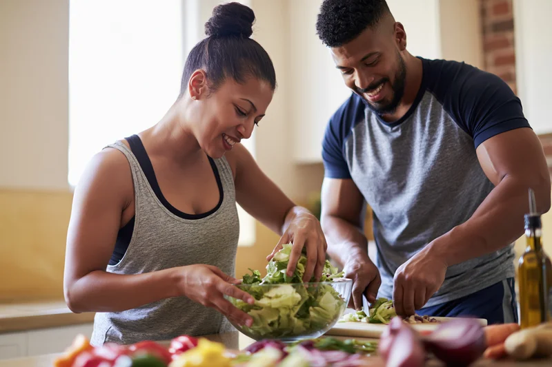 Young couple preparing fresh vegetable salad together in kitchen