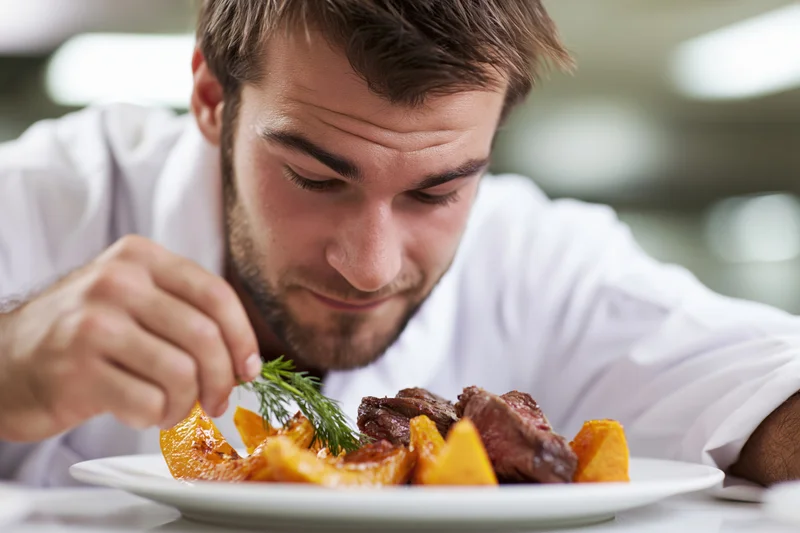 Male chef garnishing a plated dish with dill in a restaurant setting