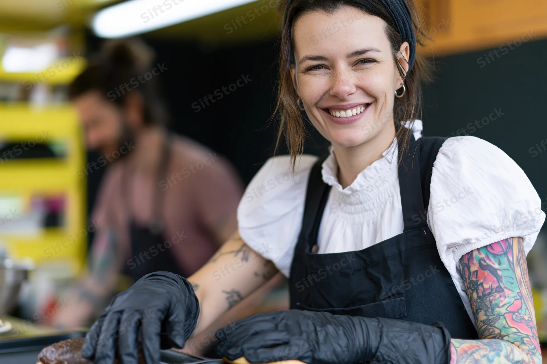 Smiling woman in apron and gloves preparing food in a small kitchen stall