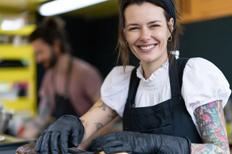 Smiling woman in apron and gloves preparing food in a small kitchen stall