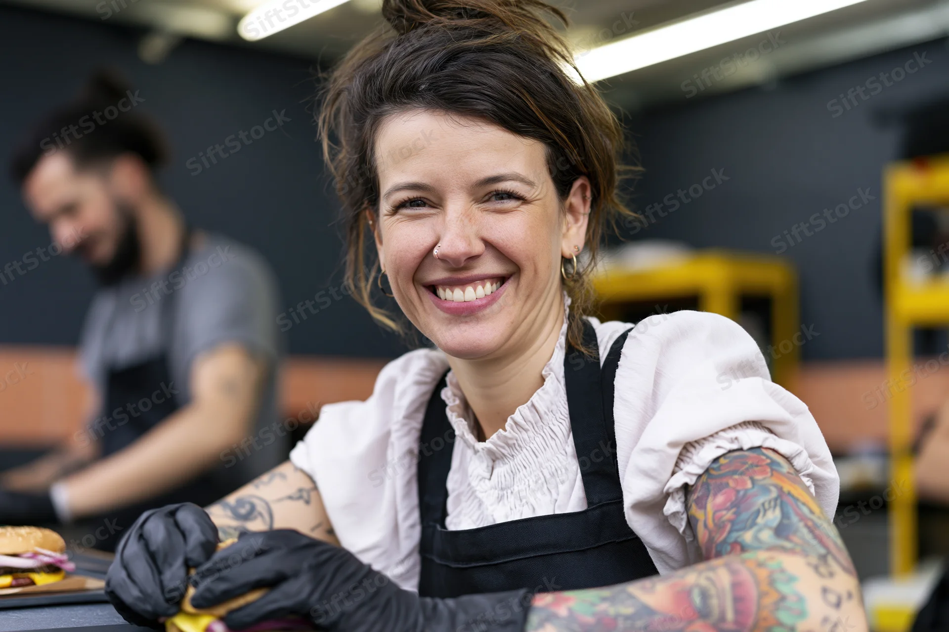 Woman in apron and gloves smiling while preparing food in a kitchen