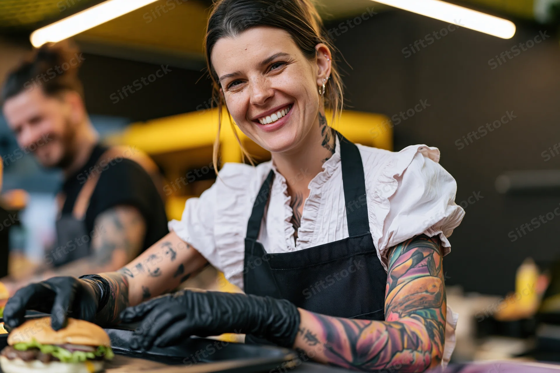 Woman chef smiling while preparing a burger in a food stall kitchen