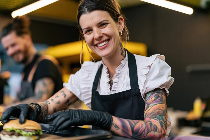 Woman chef smiling while preparing a burger in a food stall kitchen