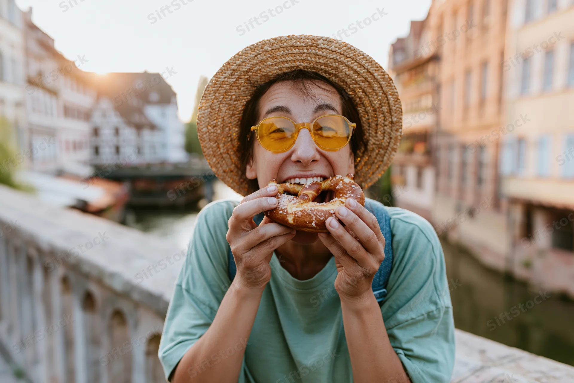 Woman eating a large soft pretzel on a stone bridge over a canal in a european city