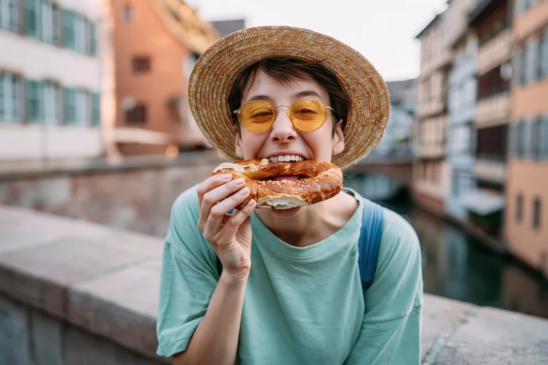 Woman eating a large soft pretzel on a stone bridge over a canal in a european city