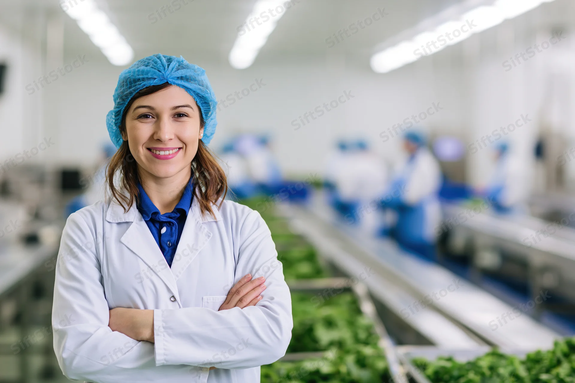 Woman in labcoat and hairnet standing with arms crossed in food factory production line