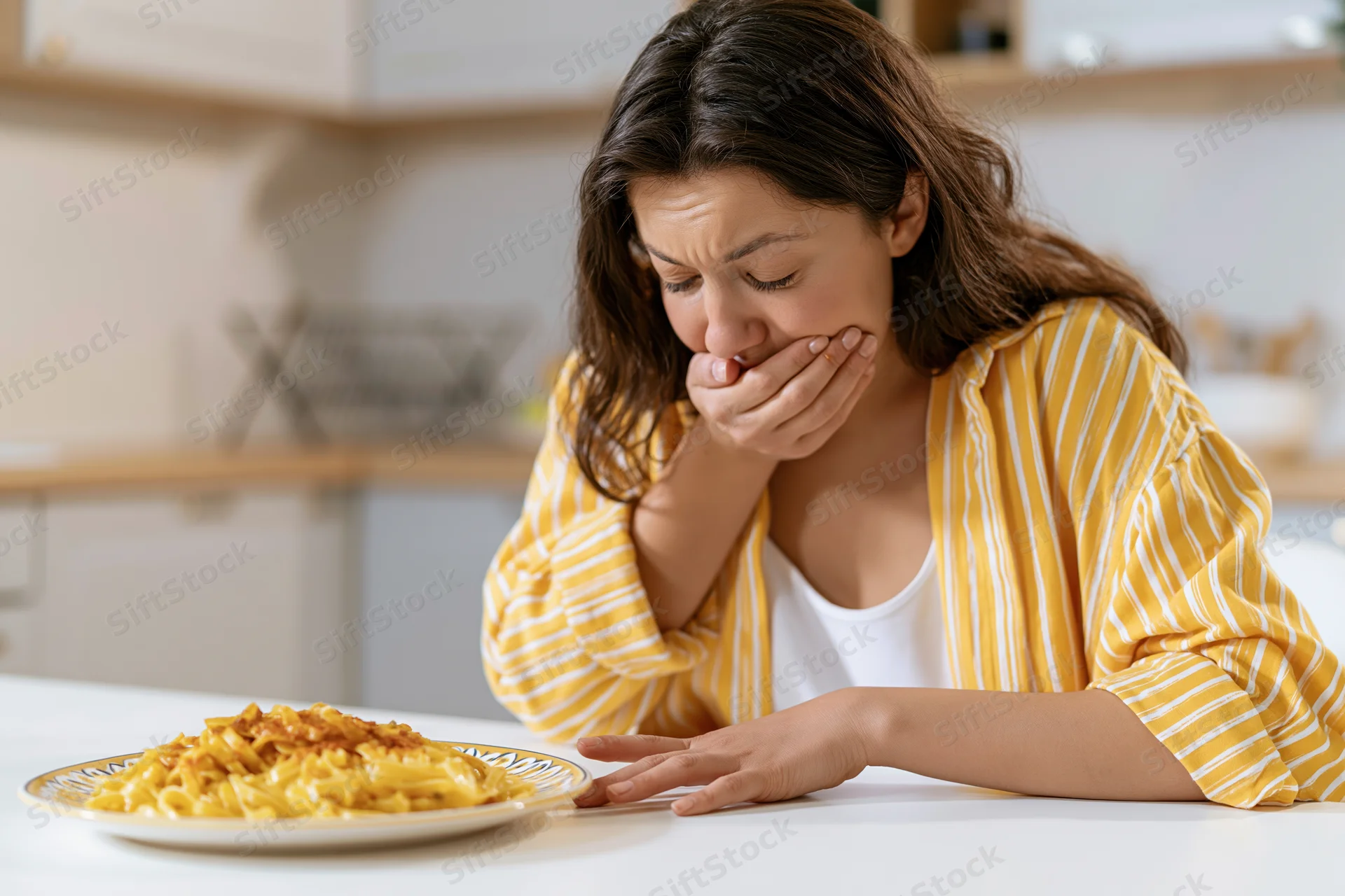 Woman covering her mouth in disgust at a plate of pasta on a kitchen table