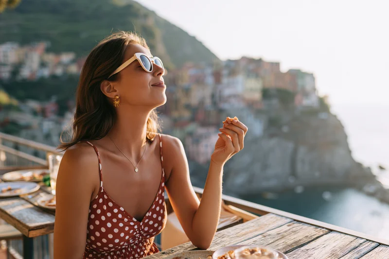 Woman sitting at outdoor terrace table enjoying snack with coastal view