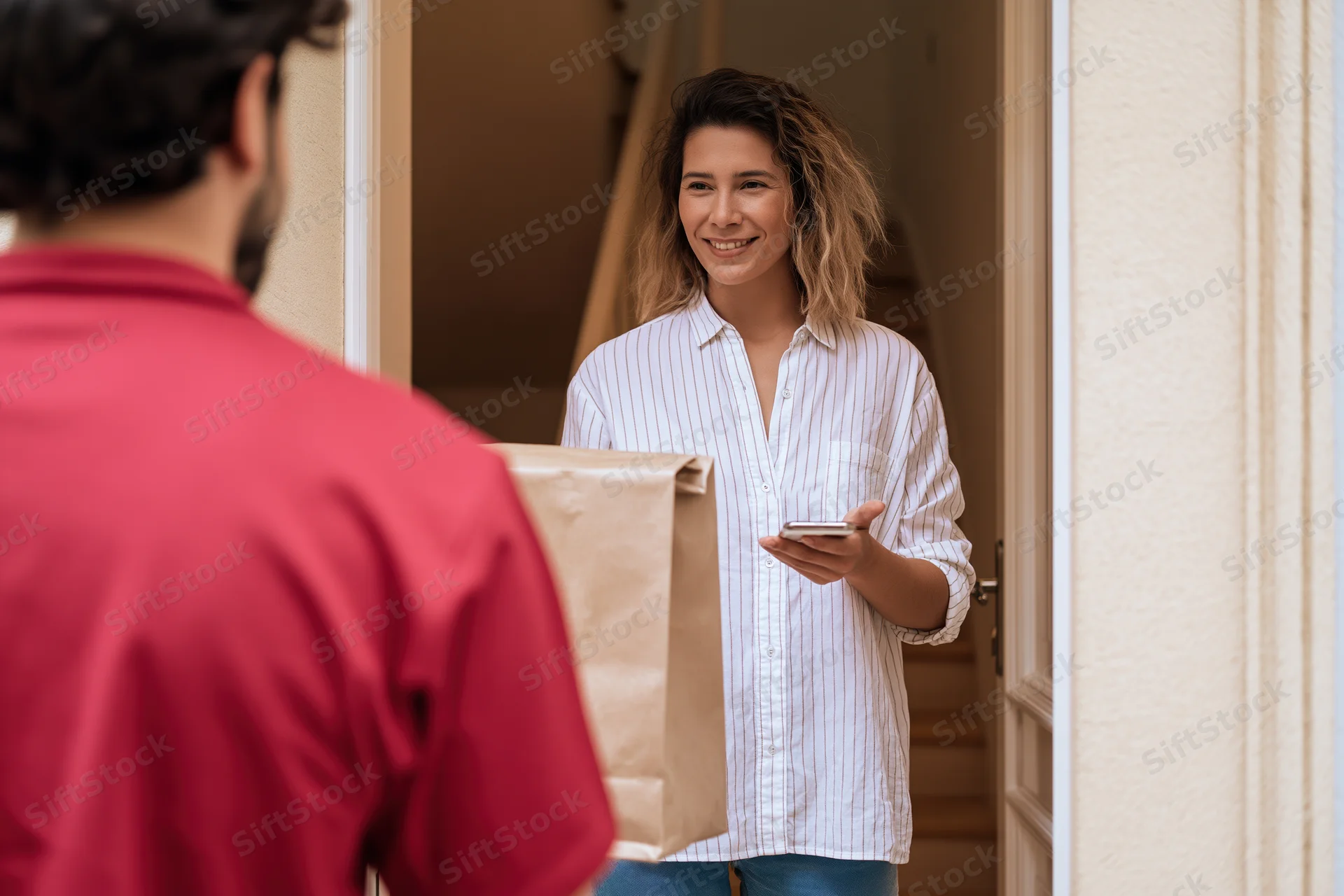 Woman smiling and receiving a brown paper delivery bag at her front door