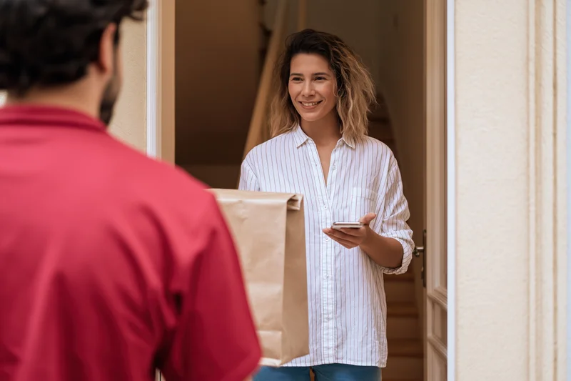 Woman smiling and receiving a brown paper delivery bag at her front door