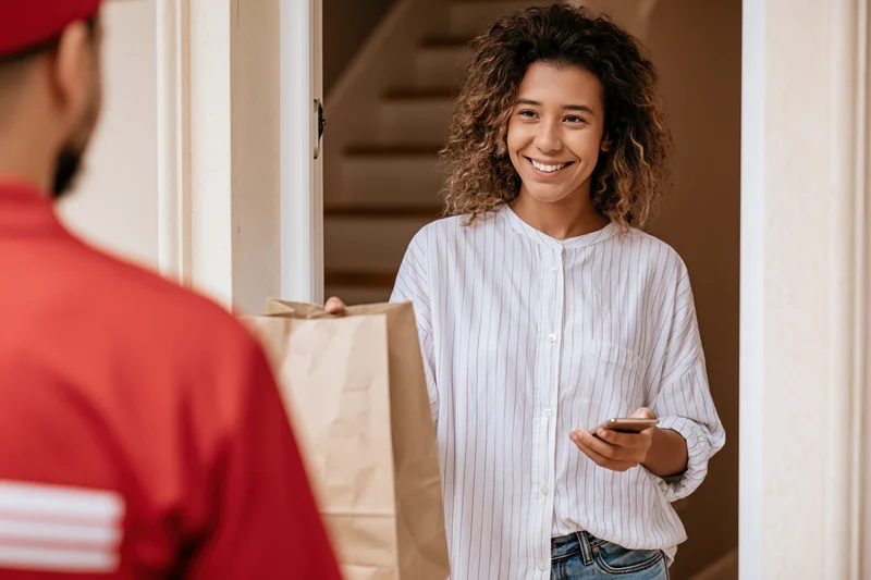 Woman smiling while receiving a brown paper delivery bag at her door