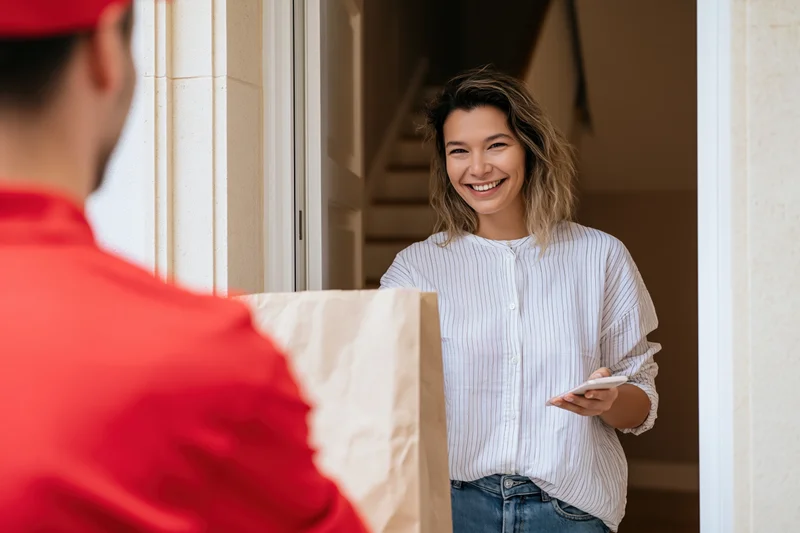 Woman smiling while receiving a paper bag delivery at her home door