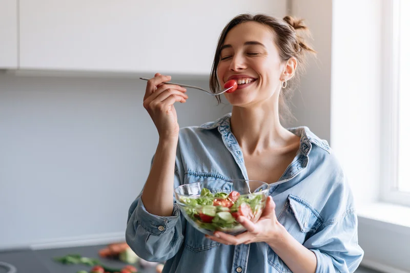 Woman eating salad with fork in modern kitchen