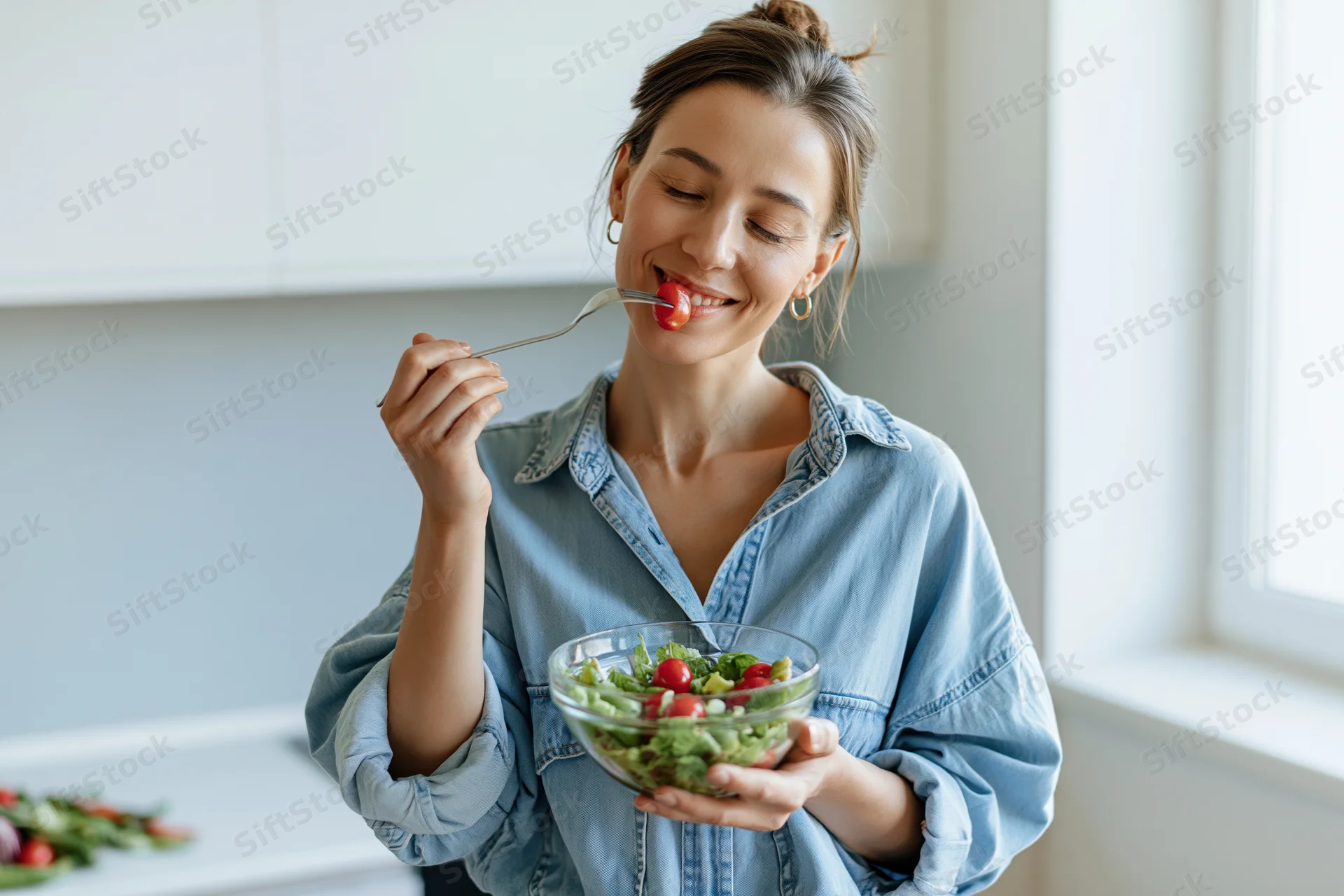 Woman eating salad with fork in modern kitchen