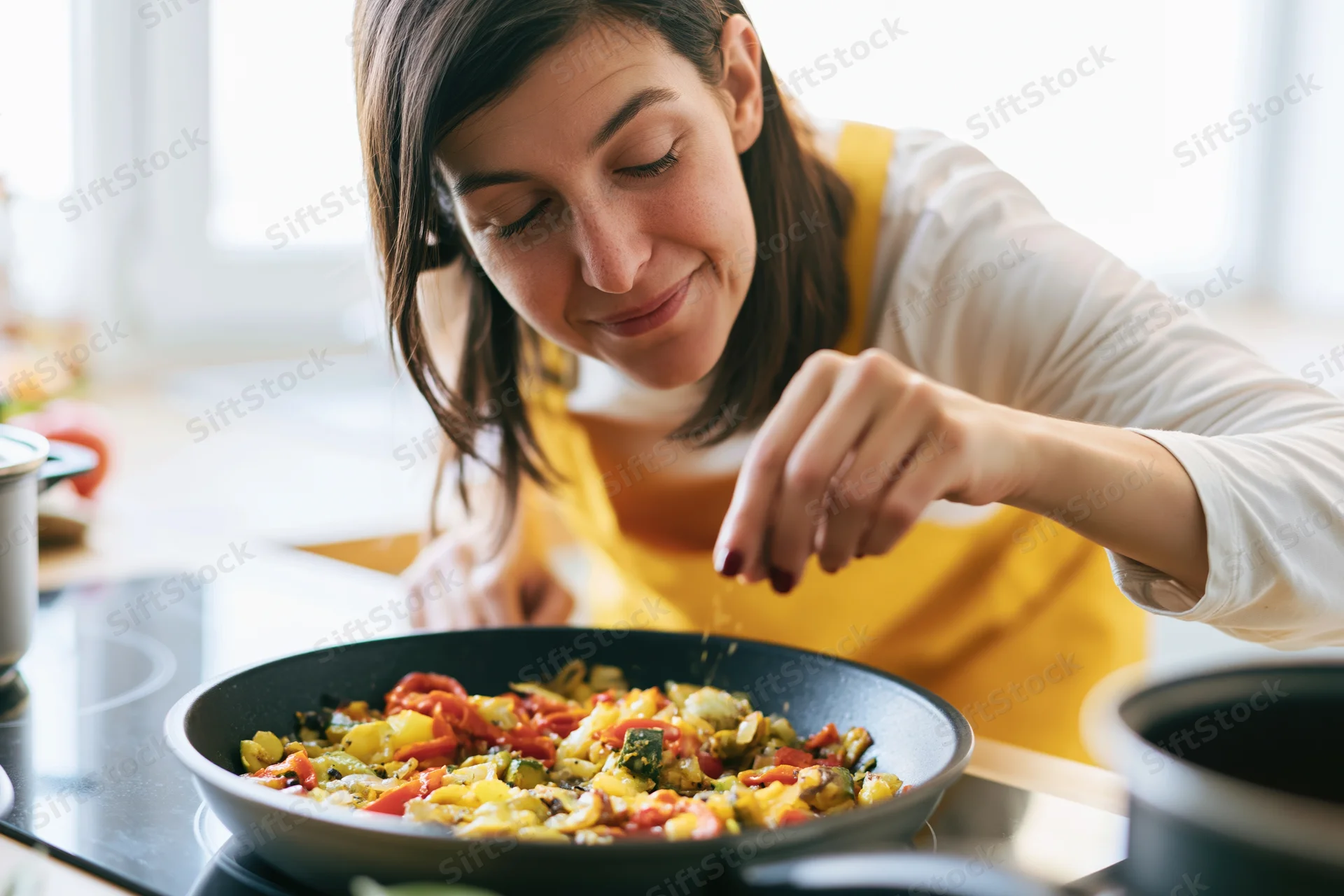 Woman sautéing colorful vegetables in a pan on a kitchen stove