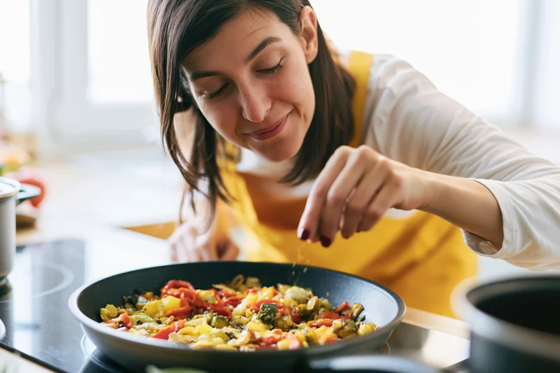 Woman sautéing colorful vegetables in a pan on a kitchen stove