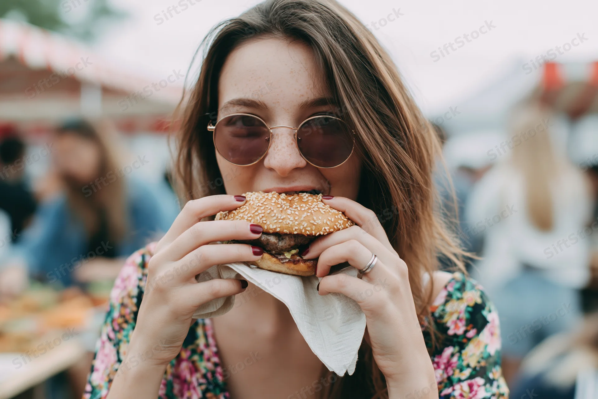 Woman biting into a sesame seed burger at an outdoor festival
