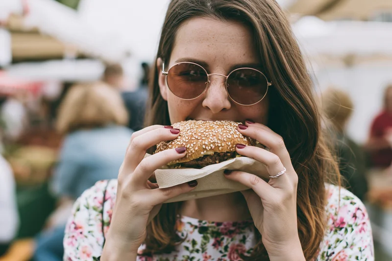 Young woman biting into a sesame seed burger at an outdoor festival
