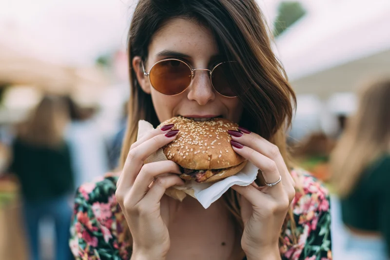 Woman biting into a sesame seed burger at an outdoor market