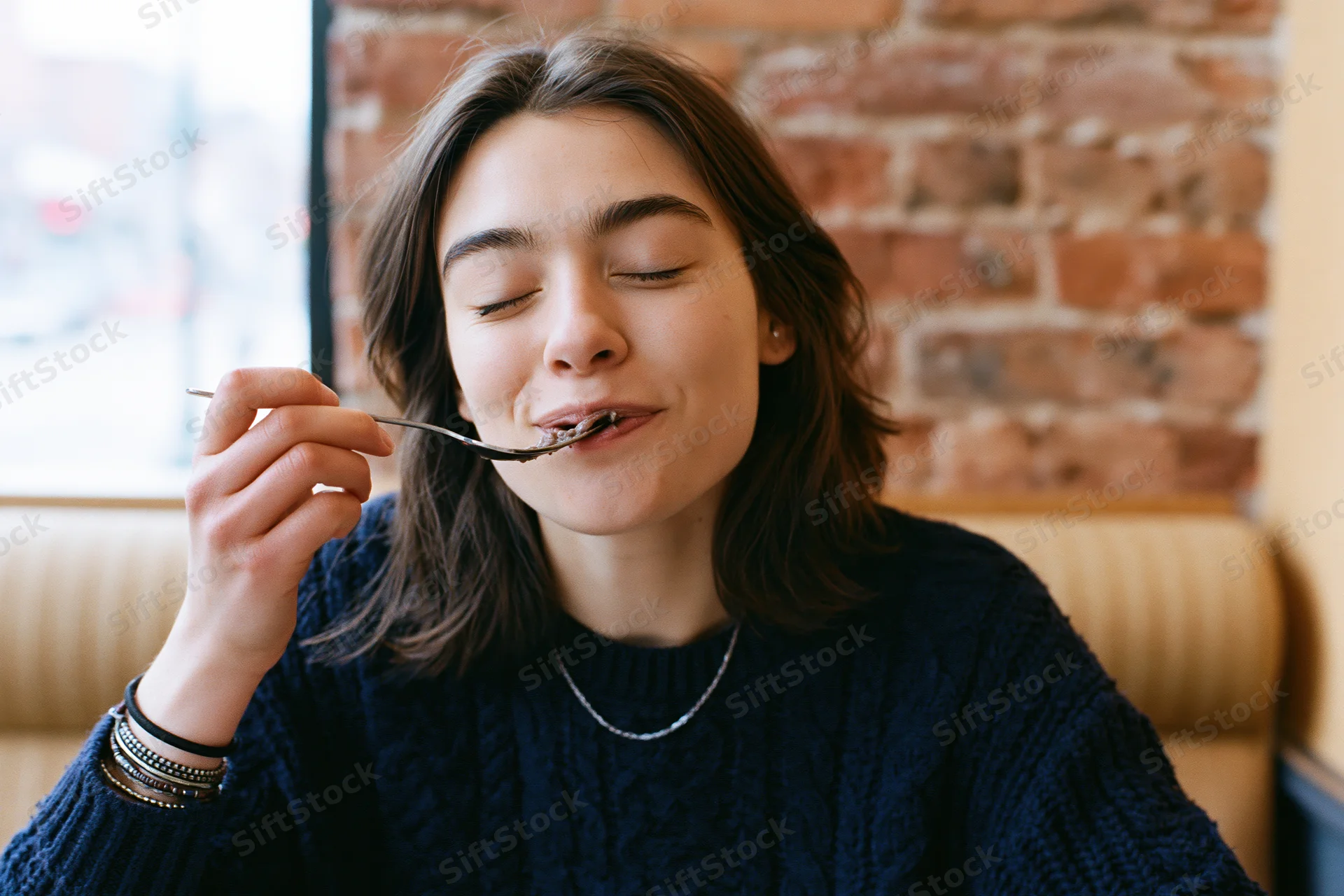 Young woman eating with eyes closed in a cafe booth