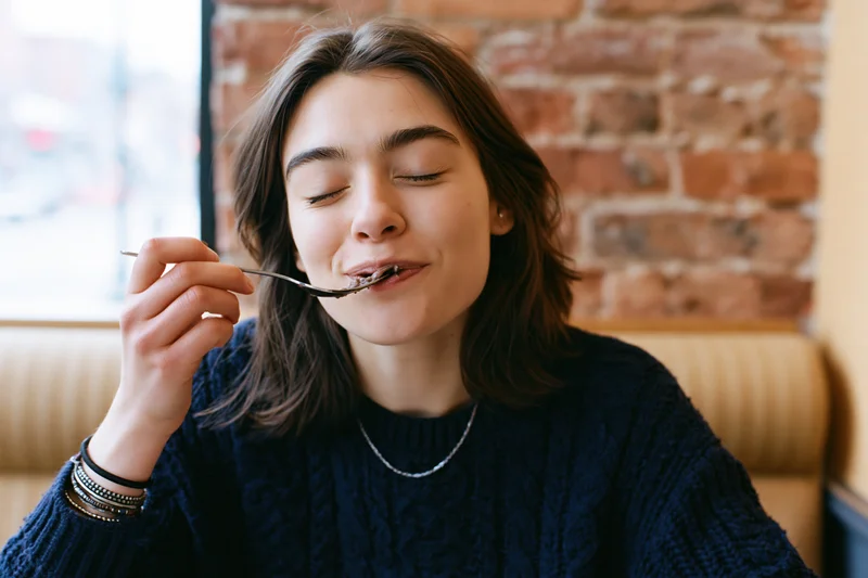 Young woman eating with eyes closed in a cafe booth