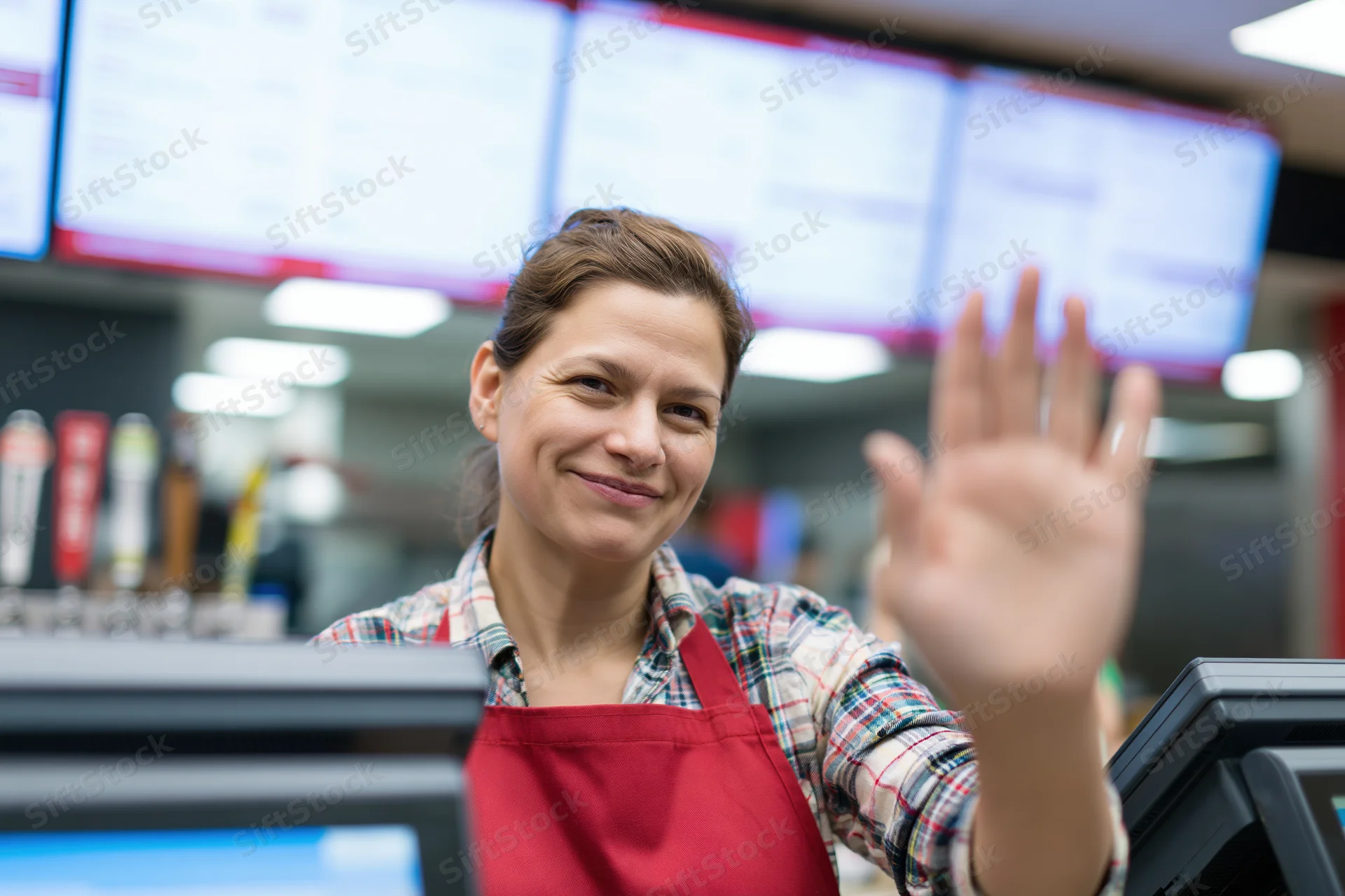 Woman cashier waving at camera behind fast food counter