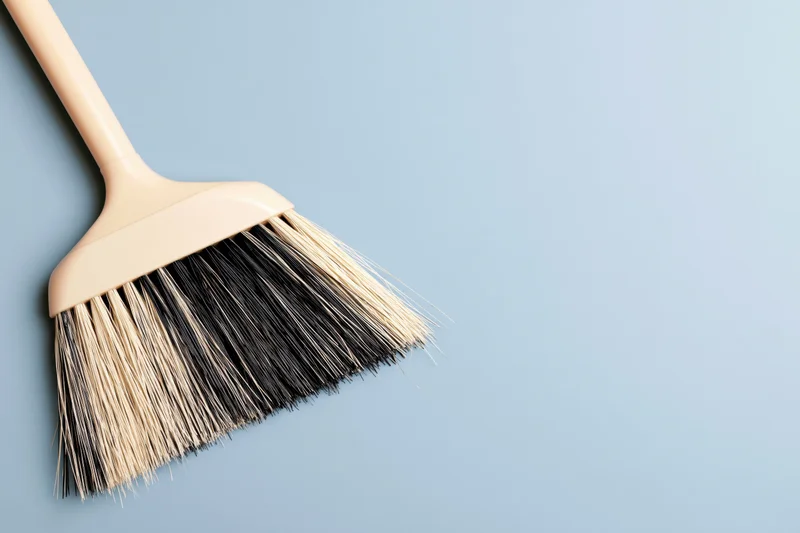 Beige plastic broom with black and cream bristles on a blue background
