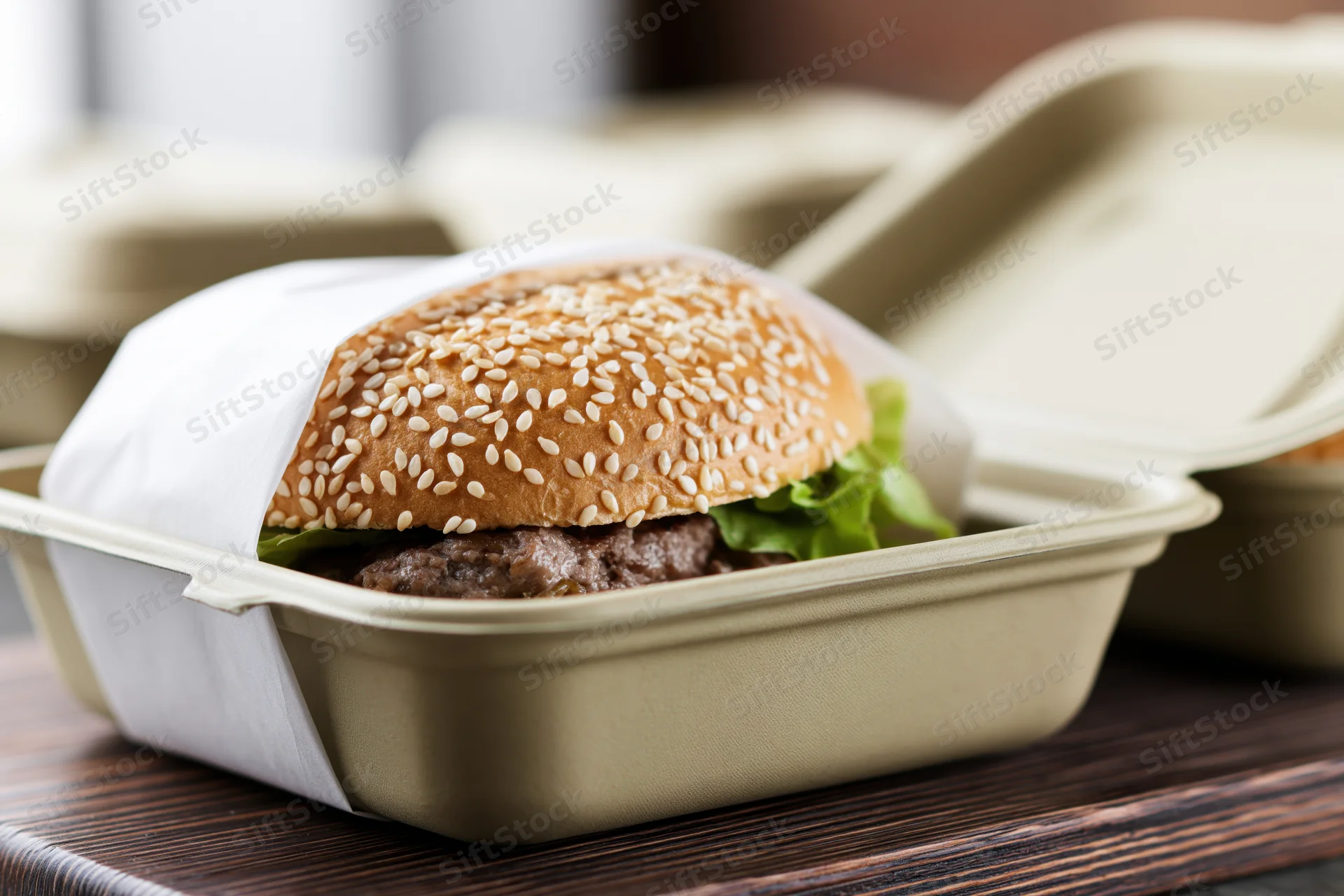 Beef burger with sesame seed bun and lettuce in open takeout container on wooden surface