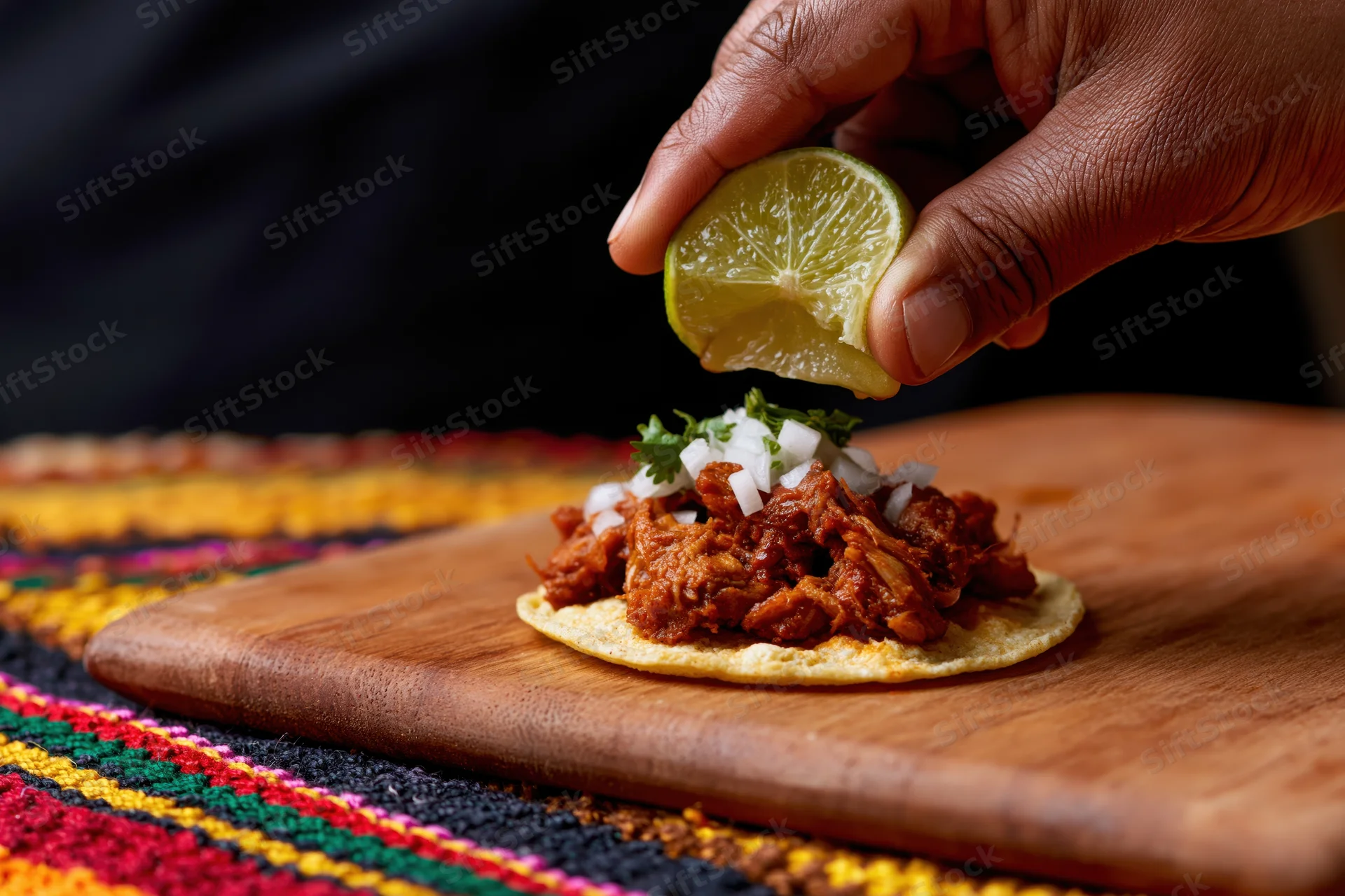 Hand squeezing lime over taco with meat and cilantro on wooden cutting board