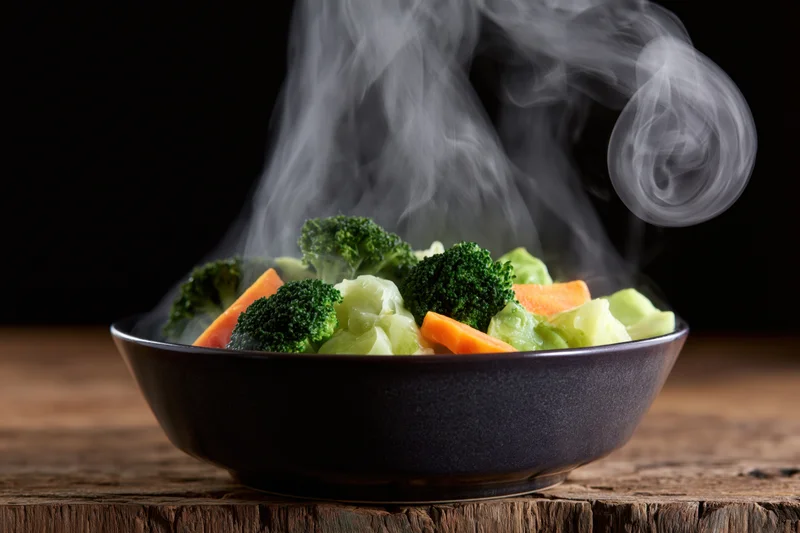 Steamed mixed vegetables in a dark ceramic bowl on a wooden table